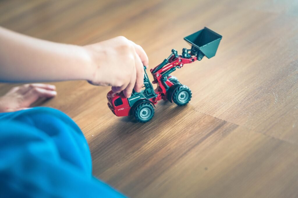 A child plays with a toy excavator on a wooden floor, enjoying creative indoor playtime.